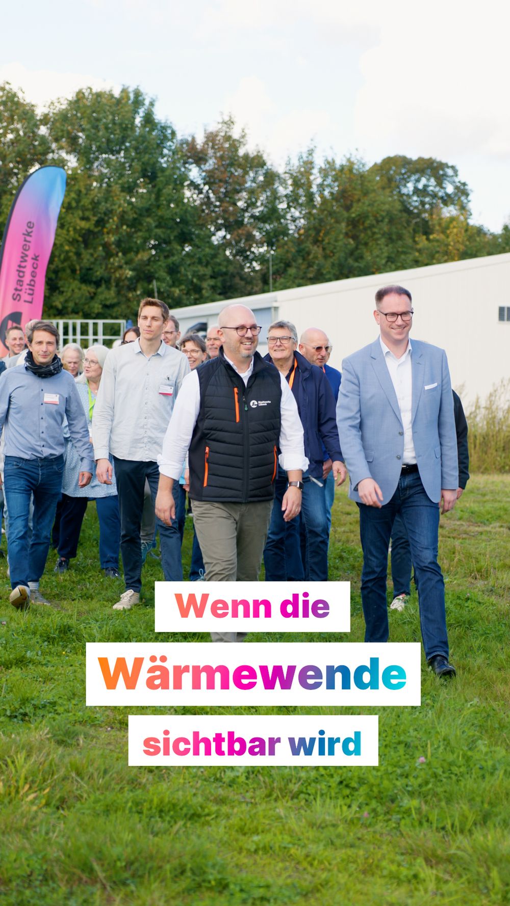 Eine Gruppe von Menschen gehen auf einer Grasfläche vor einem Gebäude