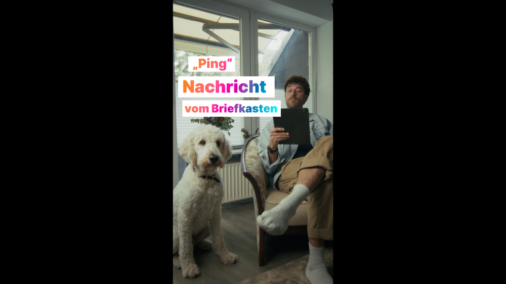 Ein Mann sitzt drinnen mit einem Tablet neben einem flauschigen weißen Hund.