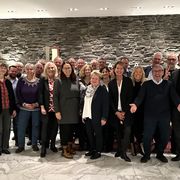 A group of people posing together indoors in front of a stone wall, some smiling and others gesturing with open arms.