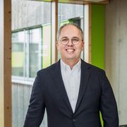 CEO Jens Meier steht an Geländer vor Fenstern und lächelt in die Kamera