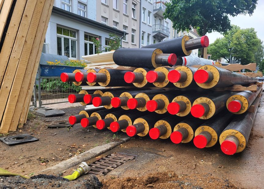 Auf einer Baustelle liegen große schwarze Fernwärme-Rohre mit roten Kappen.