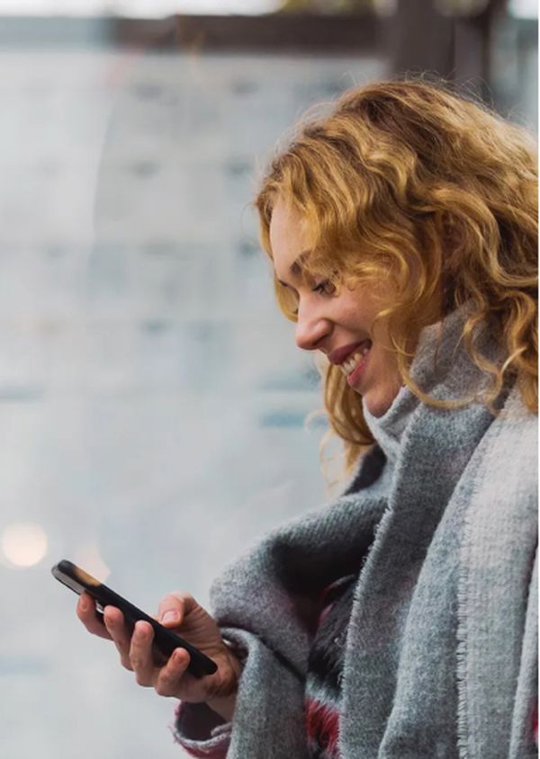 Frau an der Bushaltestelle schaut aufs Handy